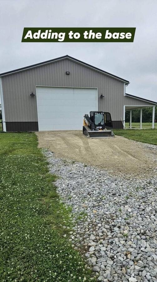 Skid steer adding gravel base to a driveway in front of a pole barn