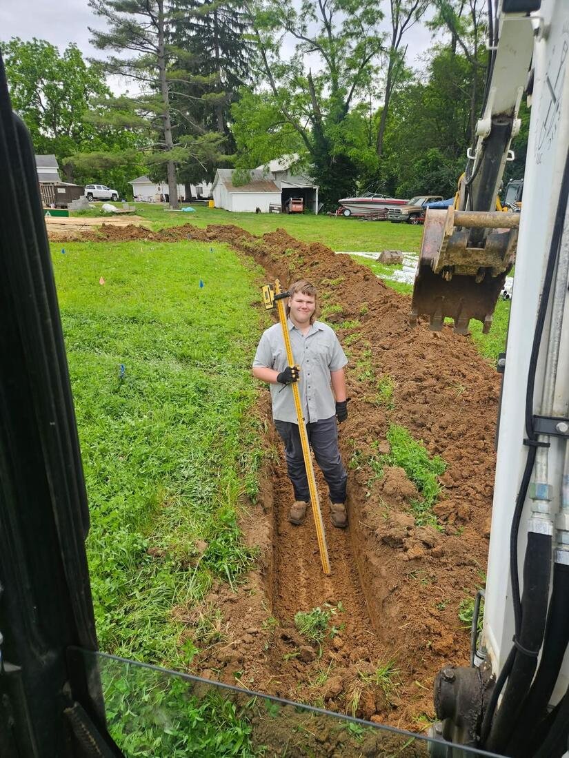 Crew member checking trench depth with a grade rod before laying pipe